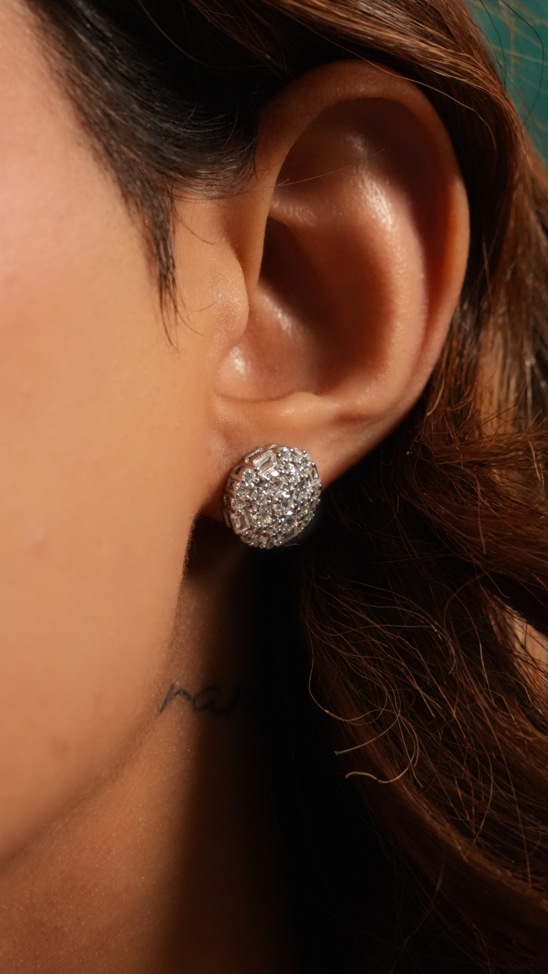 A close-up of a person's ear wearing a round, diamond-paved silver stud earring.